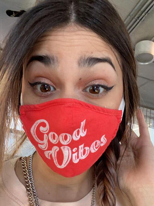 A person wearing a red face mask with "Good Vibes" written on it in white text, looking directly at the camera with wide eyes—perfect for a Before and After Gallery Vancouver feature.