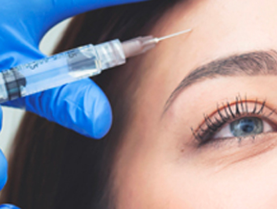 A person wearing a blue glove holds a syringe near the forehead of a woman, preparing for an injection near her eyebrow as part of Medical Services Vancouver.