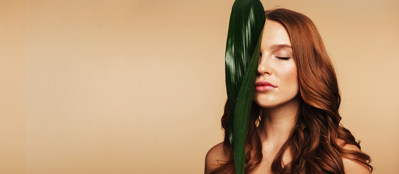 A woman holding a green leaf over her face.